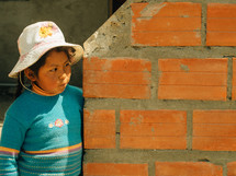 A boy stands at the end of an orange brick wall.
