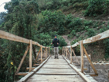 A man stands on a wooden pedestrian bridge.