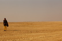 man standing in a desert wrapped in a blanket