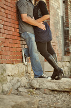 Embracing couple leaning against a brick wall.