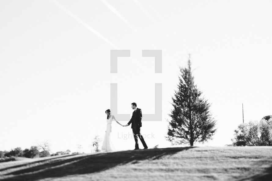 bride and groom holding hands at the top of a hill 