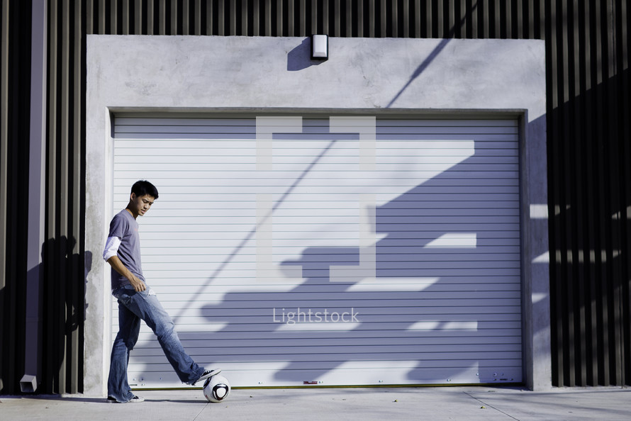 Boy standing outside closed garage door with foot on soccer ball.