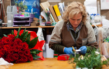 Florist with professional clothing in a nursery. Preparation of a bouquet of red roses.