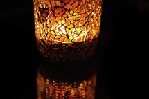 light from a burning candle through mosaic glass candle holder