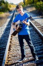 teen boy playing a guitar on railroad tracks 