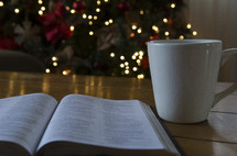 mug and open Bible on a coffee table and Christmas tree in the background 