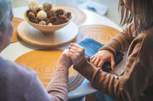 Elder woman with her daughter holding hands together and praying at the table