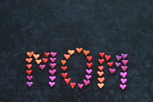 the word MOM written with many little colorful clay hearts on black background