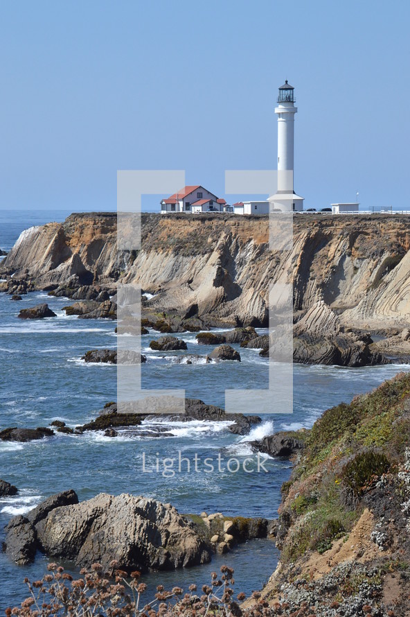 A lighthouse on a peninsula with cliffs. 
lighthouse, shore, ocean, sea, light, white, shipping, navigation, boat, safe, secure, reliable, preservation, ship, ships, sky, blue, horizon, skyline, rocks, rock, stone, stones, cliff, cliffs, danger, dangers, dangerous, warning, caution, premonition, advance notice, advisory, caveat, admonition, warn, alert, admonish, save, safeguard, guard, rescue, protecting, protect, protection, coast, seaside, shoreline, seashore, seacoast, waterside, coastline, seafront, ragged, jagged, rugged, forbidding coastline, stony, craggy, bouldery, water, wave, waves, sand, house, tower, high