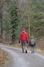 a man and a child walking together on a path through a forest 