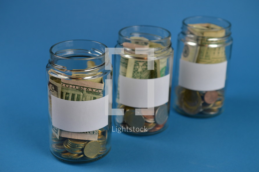 three savings jars full of money with blank labels on cyan background