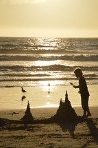 A child builds a sand castle on the beach in the light of the sunset.
