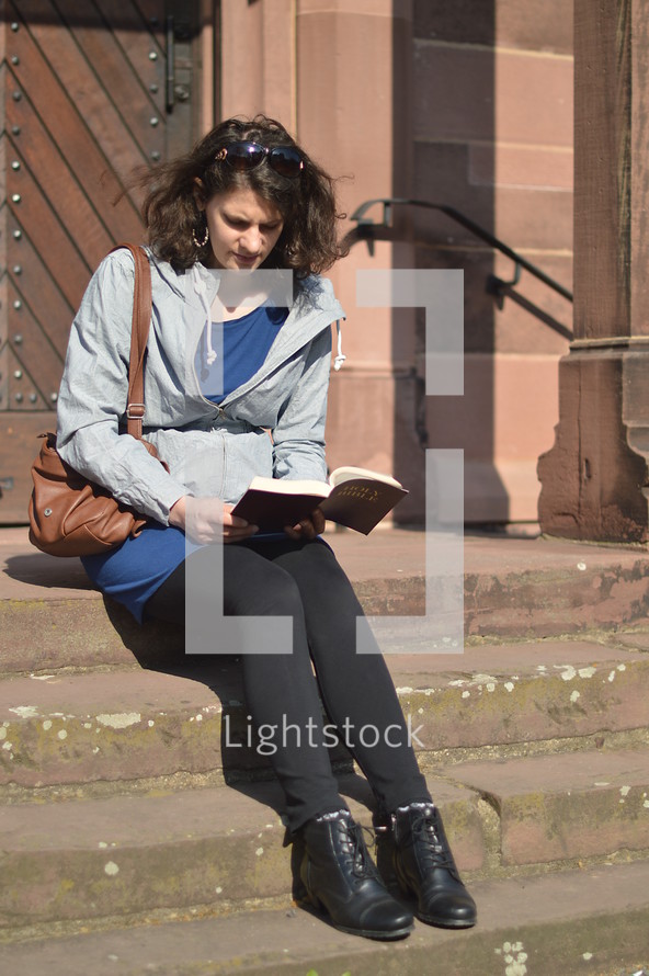 a woman sitting and reading a Bible on church steps 