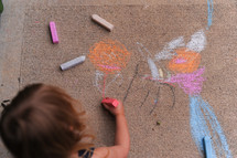 a toddler girl coloring with sidewalk chalk 