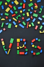 the letters VBS out of colorful wooden toy blocks on black background 