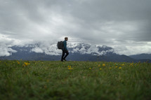 Man hiking with backpack in grass and yellow flowers
