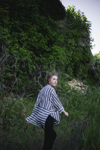 a woman in a flowing shirt walking through tall grass 