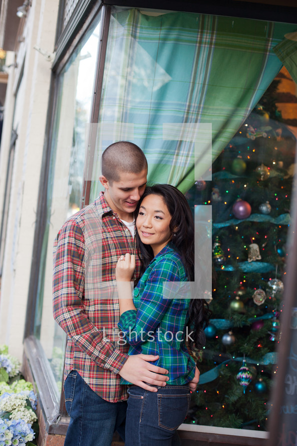 couple hugging in front of a Christmas tree in a store window