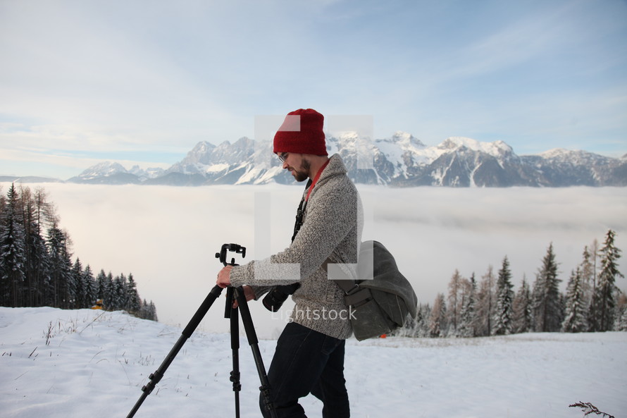 man with a tripod and camera standing outdoors in snow 