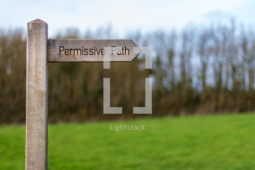 A wood trail sign points the way of the "Permissive Path" with trees and a meadow in the background