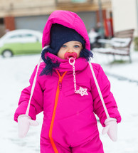 Adorable toddler baby girl in a magenta snow suit playing on the snow.