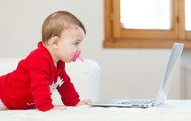 Eight months old baby girl using a laptop on the couch at home