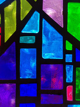 A close-up view of a stained glass window panel with vivid shades of blue, green and purple colors adorning a church sanctuary. 