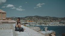 a woman sitting on a stone wall with a marina in the background 