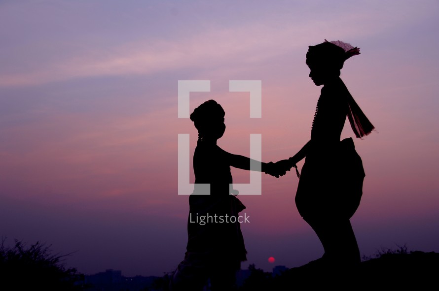 silhouette of children holding hands against a purple sky