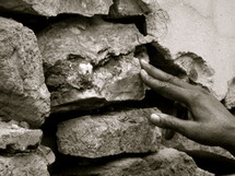 hand placing a stone in a wall