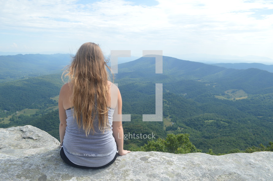 a woman sitting on a mountaintop looking out 