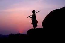 silhouette of a boy holding a stick at sunset 