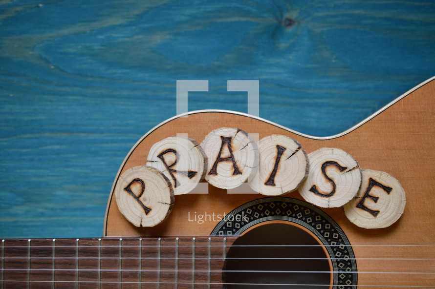 guitar on teal wooden background with wood pieces on it lettering the word: PRAISE