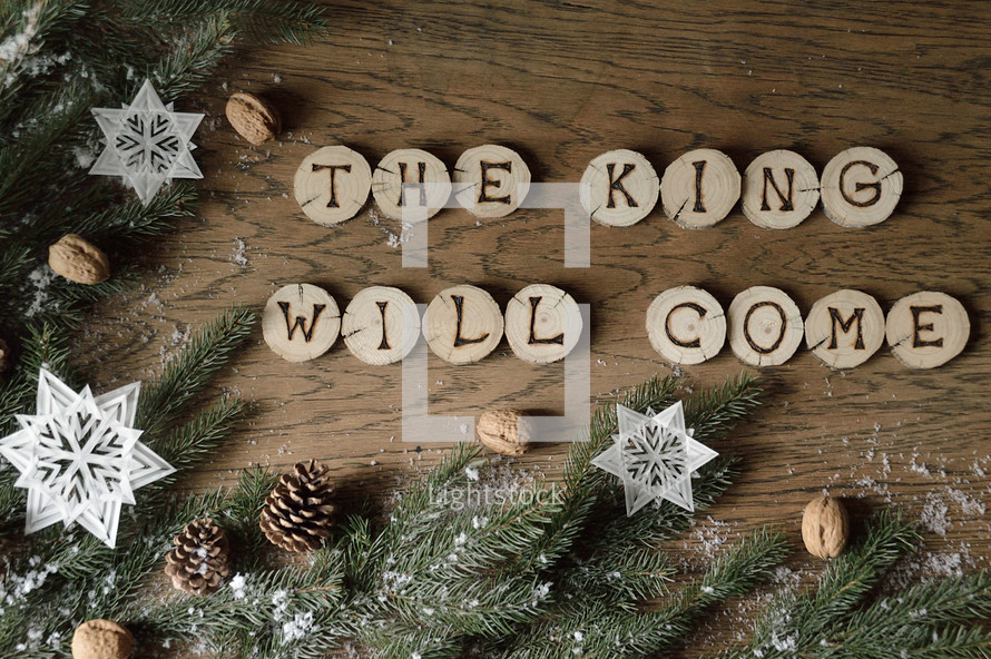 star ornaments, pine cones, snow, pine boughs and the words THE KING WILL COME on wooden slices
