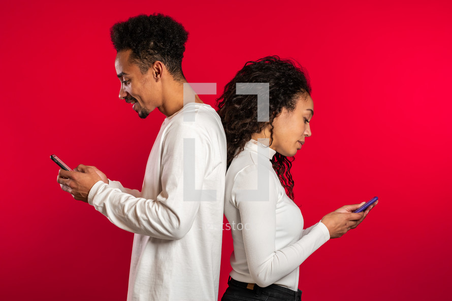 african couple stand with their backs to each other and print messages or surf the Internet from their mobile phone. Technology, smartphone, social networks concept.