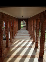 A long hall or corridor shows archways where columns of sunlight penetrate and light the path of this hallway in a church in the southeastern United States. 