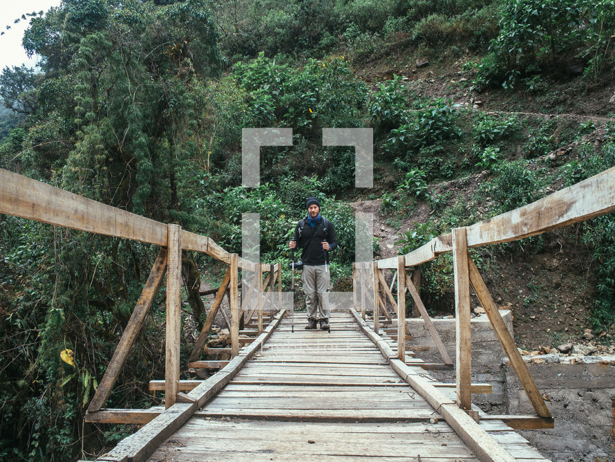 A man stands on a wooden pedestrian bridge.