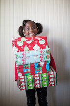 a girl child holding a stack of Christmas gifts 