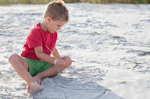 boy child drawing in the sand on a beach 