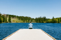 a man sitting at the end of a dock 