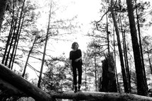 a woman standing on a fallen tree in a forest 