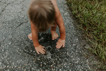 a toddler in a diaper splashing in a puddle 