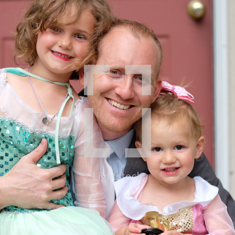 a father hugging his daughters dressed as princesses 