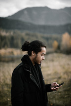 A man looking at his cellphone screen standing in a field 