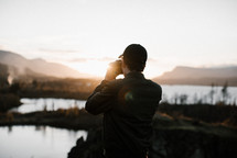 a man taking a picture of a lake at daybreak 