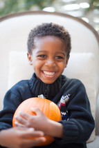a smiling child holding a pumpkin 