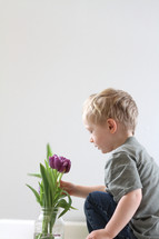 toddler boy touching flowers in a vase 