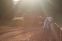 sunlight shining down and a bride and groom walking down a dirt road 