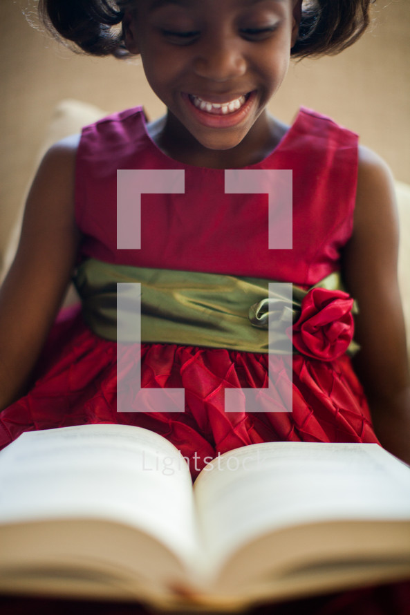 a girl child in a red Christmas dress reading a Bible 