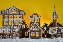 home made gingerbread village in front of yellow background on white snowlike velvet as advent decoration